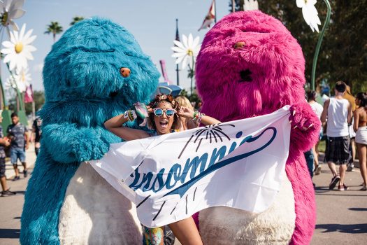 Two furry performers with a smiling Headliner and an Insomniac flag