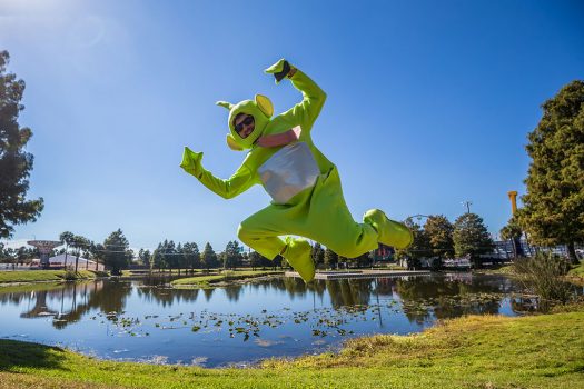 A Headliner in a Teletubby costume jumping by a pond